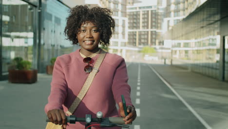 Fröhliche-Afroamerikanische-Frau-Posiert-Mit-E-Scooter-Und-Telefon-In-Der-Stadt